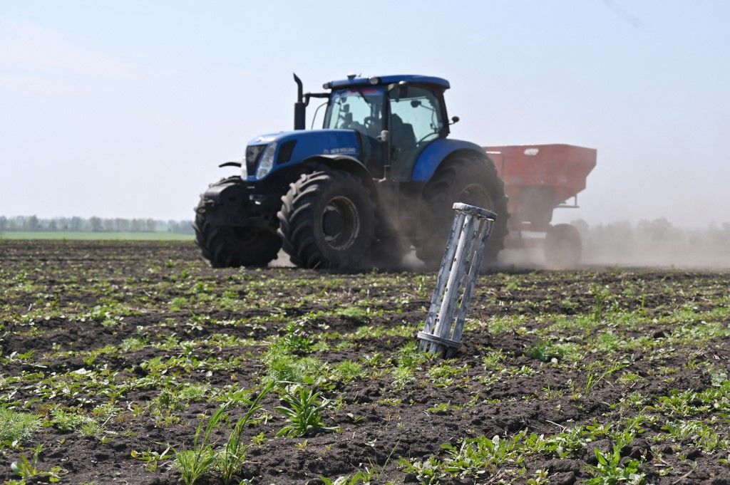New Holland traktor halad el egy orosz rakéta szántóföldbe fúródott részegysége mellett, nem messze Harkiv városától 2022. május 8-án - Fotó: AFP/Europress, SERGEY BOBOK