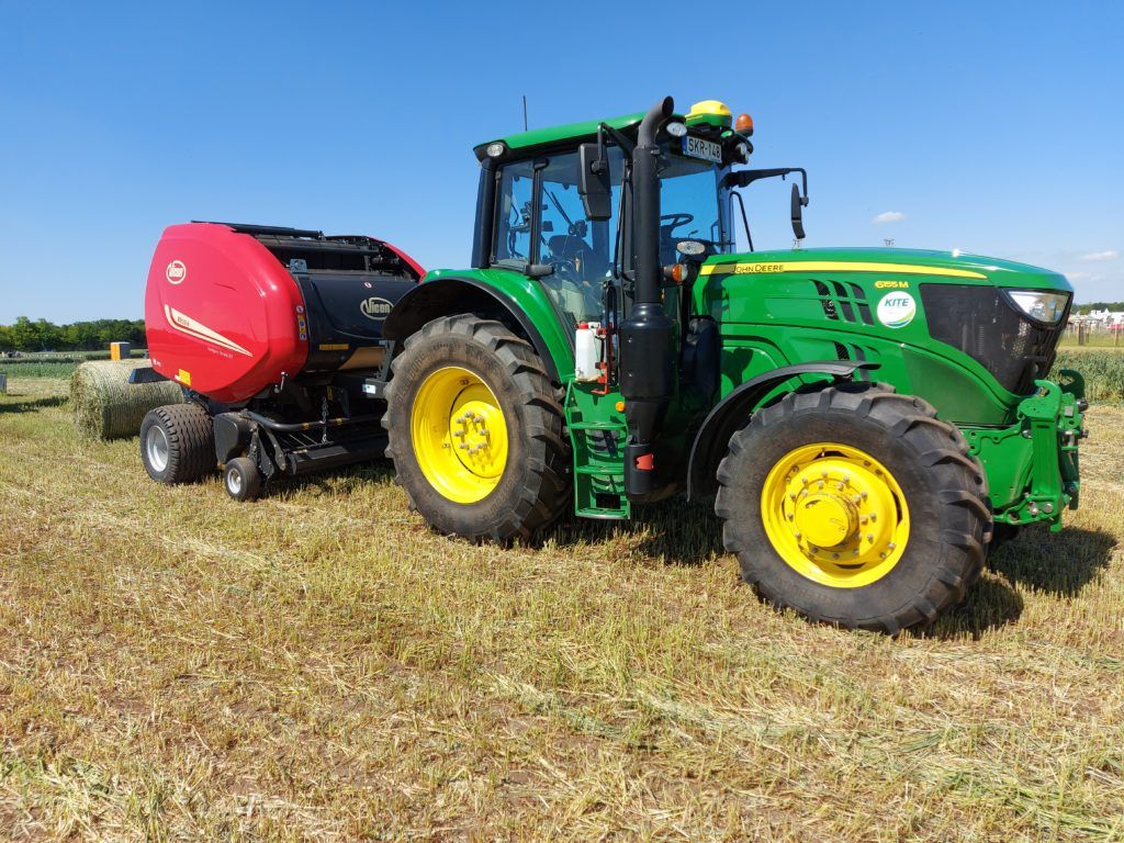 Szép piros bálázó a John Deere traktor mögött a takarmányozás szolgálatában